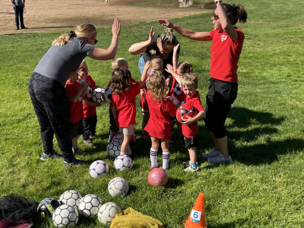 Young kids hold hands up in huddle with coaches at soccer game. Photo courtesy of Lincoln City Parks and Recreation.