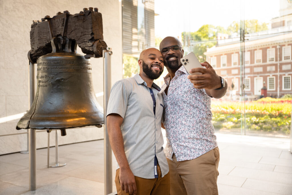 Two tourists pose to take a picture in front of the Liberty Bell