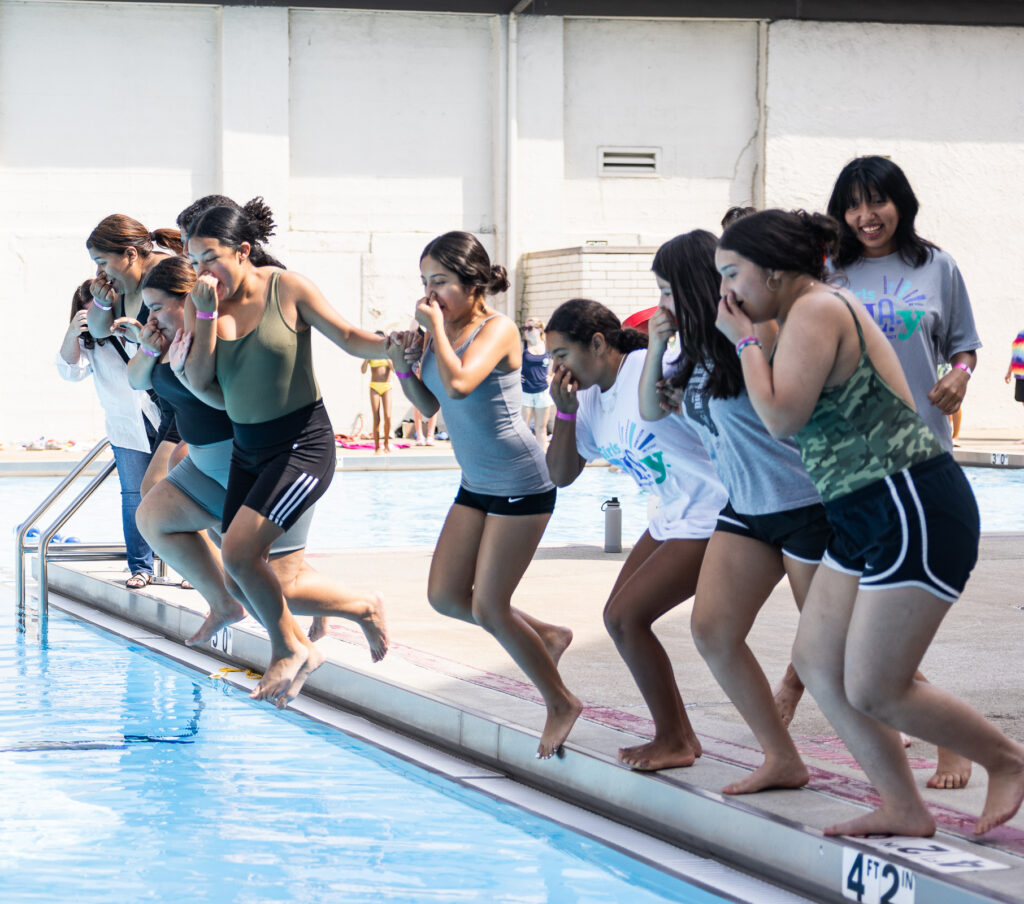 Group of youth jump into indoor pool while holding hands.