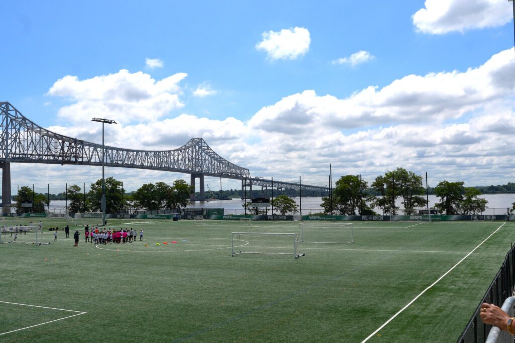Youth huddle on an outdoor soccer field along the Delaware River at the WSFS Bank Sportsplex, the Sunday site of the Youth Sports in Parks and Recreation Summit.